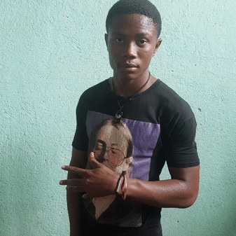 Young man wearing a black T-shirt with a graphic print, standing against a light blue wall.