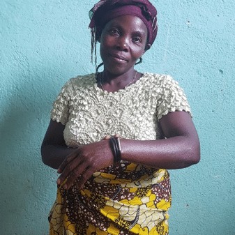Ambitious woman standing against a blue wall, dressed in traditional African attire and headwrap, showcasing confidence and resilience.