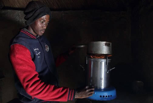 Boiled water being heated on a portable stove by a young woman in a dimly lit environment.