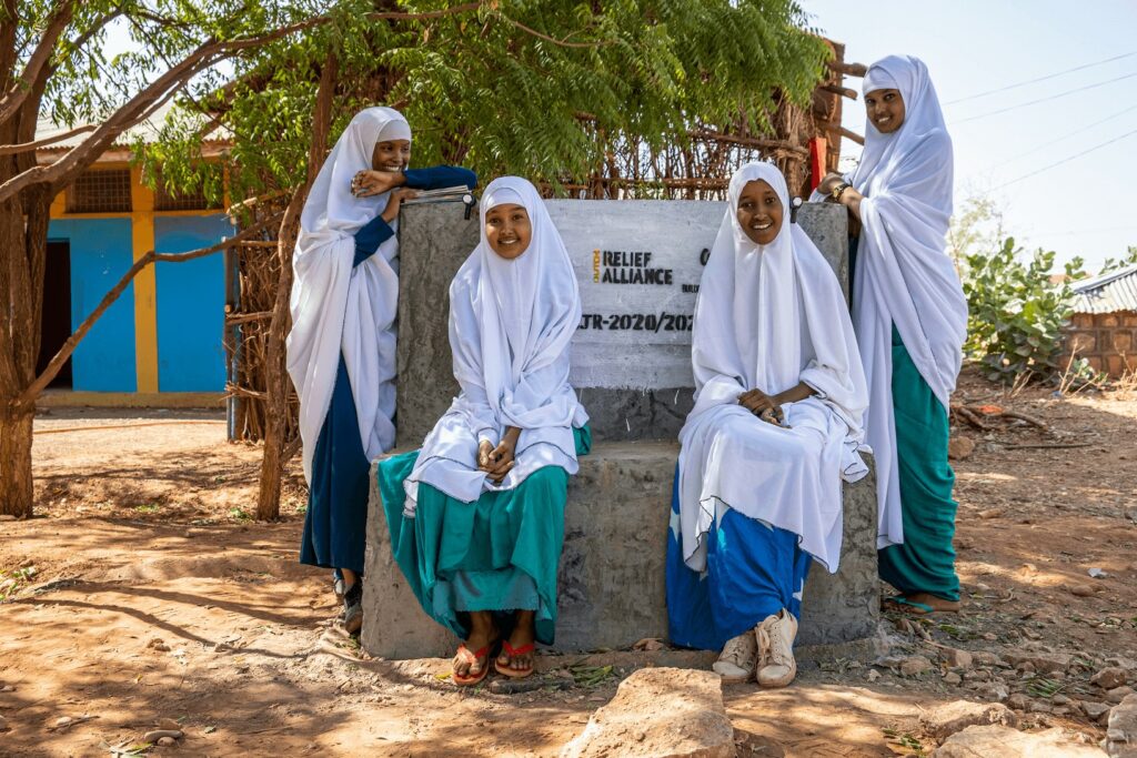 Girls in traditional Swift clothing posing around a concrete monument in a rural setting.