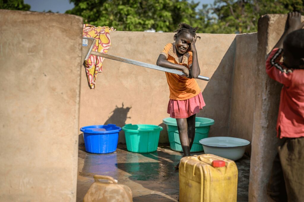 Clean water being fetched by a young girl in a developing area, with colorful buckets and water containers, demonstrating access to basic needs and community resilience.