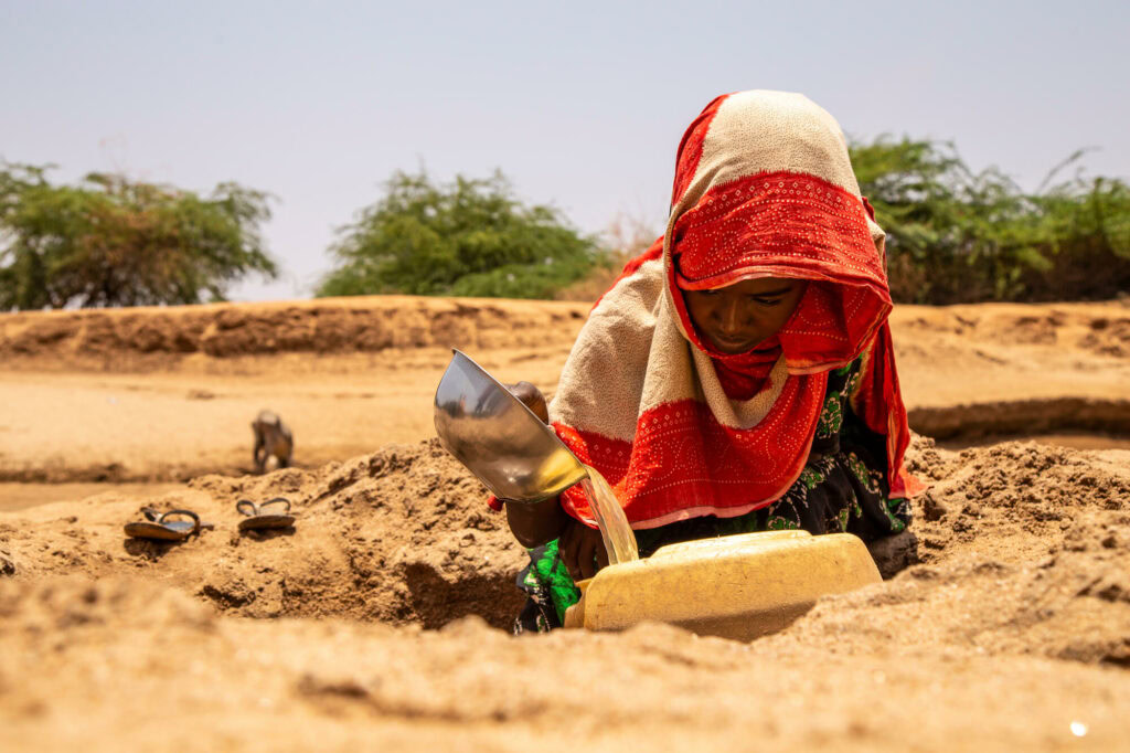 A woman in traditional clothing is collecting water from a well in a drought-affected area, highlighting the importance of emergency relief efforts by the Dutch Relief Alliance.