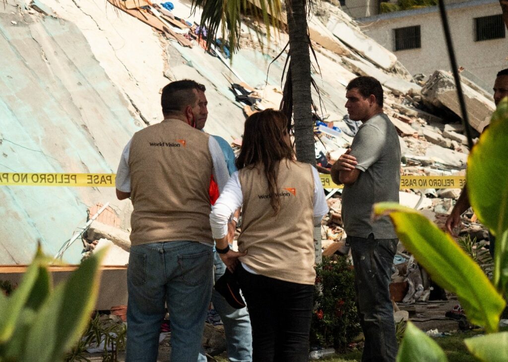 Relief workers assess damage after earthquake in Venezuela, with collapsed buildings in background.