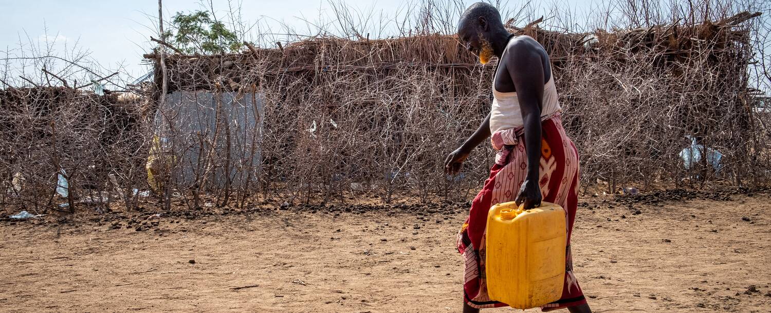 Woman carrying a yellow jerrycan across a dry compound in Ethiopia