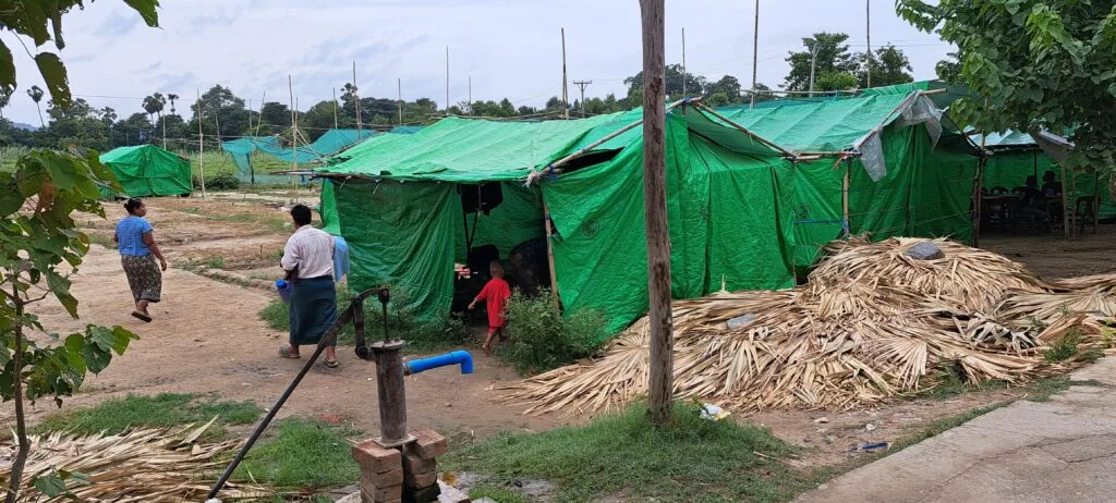Temporary shelter tents made of green tarps in a refugee camp setting.