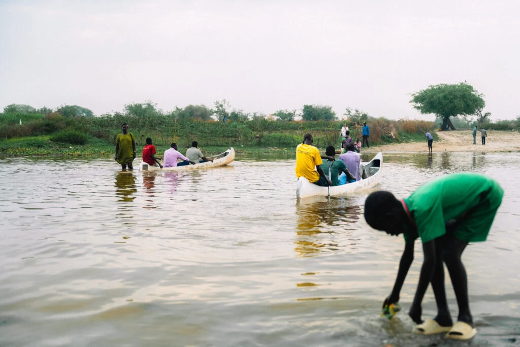 People in boats and on the shore during a flood in South Sudan.