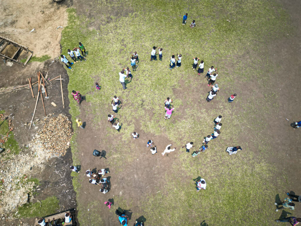 Group of children and adults forming a heart shape on a grassy field.
